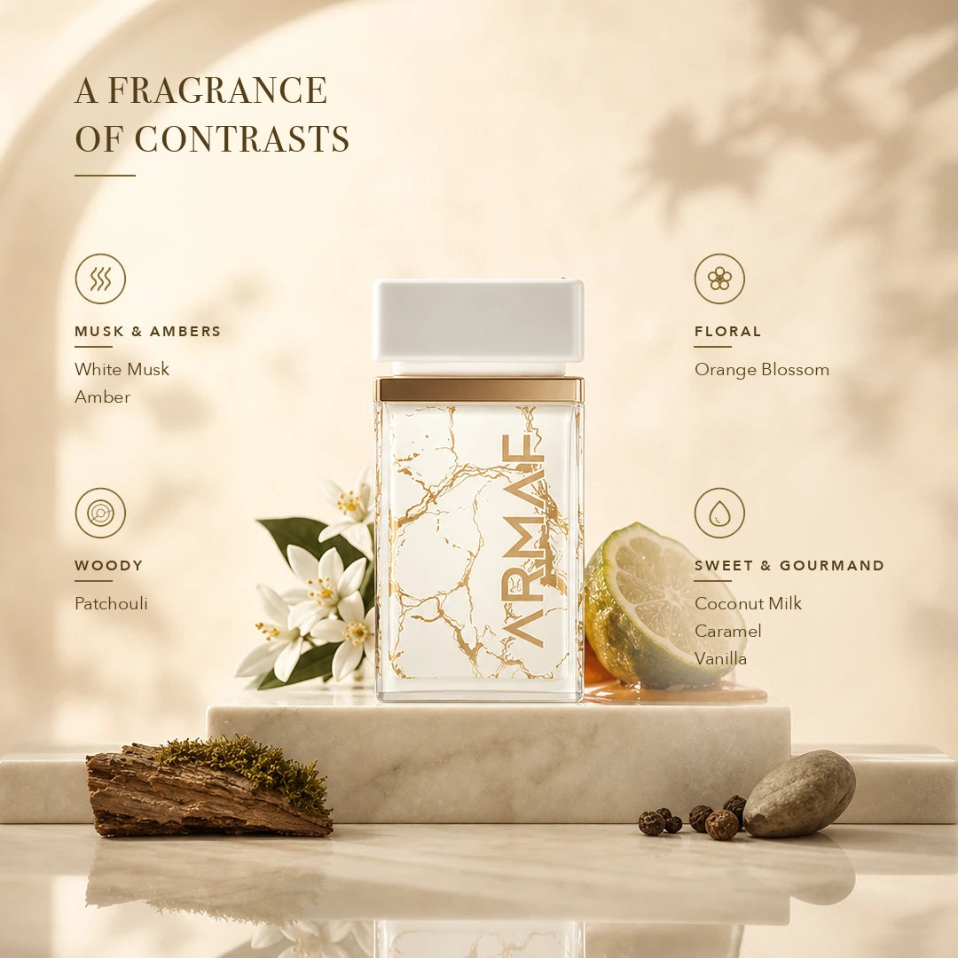 A rectangular fragrance bottle with a white cap and gold marble veining, displayed on a marble pedestal with flowers, a lime slice, and stones. Text on the image reads 'A FRAGRANCE OF CONTRASTS' and lists scent notes including Musk & Ambers, Floral, Woody, Sweet & Gourmand.